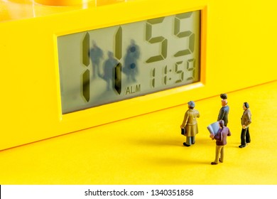 yellow alarm clock with at eleventh hour time with little miniature figurines standing in front of the alarm clock, stress, time and success concept