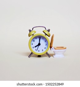 Yellow Alarm Clock And White Toilette Bowl Over Light Background, Healthcare And Wasting Time Concept 