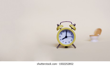 Yellow Alarm Clock And White Toilette Bowl Over Light Background, Healthcare And Wasting Time Concept 