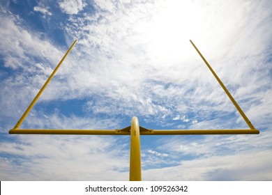 Yellow American football metal field goal against a partially cloudy sky. Viewed from below and the back of the field goal.