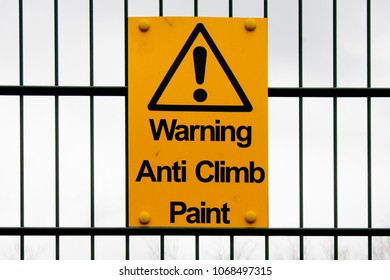 Yellow anti climb warning sign on a fence against a cloudy sky