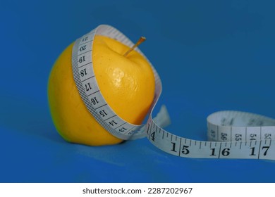 Yellow apple with measuring tape around it and blue background. health concept, healthy lifestyle concept.