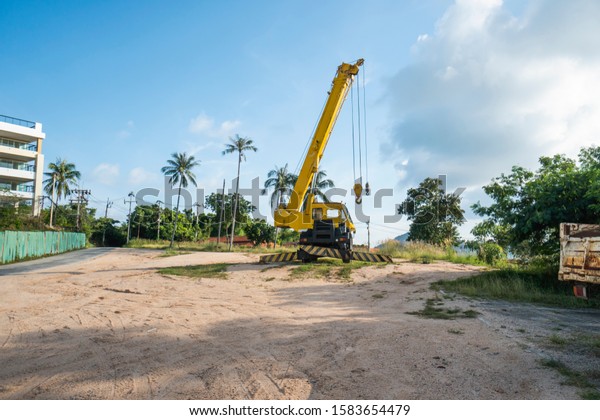 Yellow automobile crane with risen telescopic\
boom outdoors. Mobile construction crane on a constructin site.\
Crane machine stand by waiting for work under the construction\
building. Heavy\
industry.