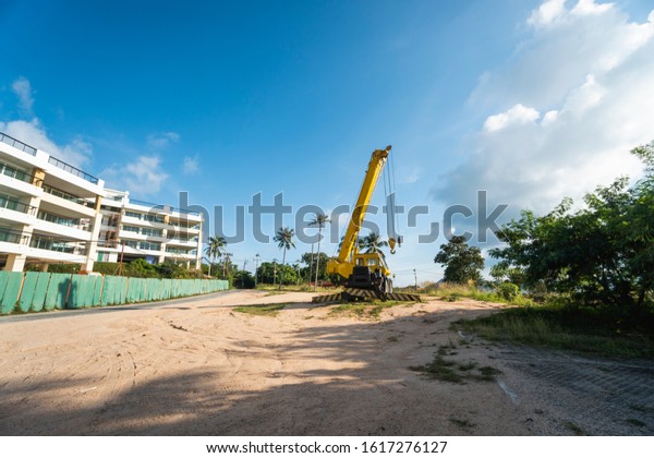 Yellow automobile crane with risen telescopic\
boom outdoors. Mobile construction crane on a constructin site.\
Crane machine stand by waiting for work under the construction\
building. Heavy\
industry.
