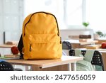 Yellow backpack with apple and copybooks on desk in classroom