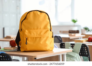 Yellow backpack with apple and copybooks on desk in classroom