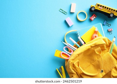Yellow backpack overflowing with school essentials such as pencils, scissors, and multicolored notebooks, complemented by a miniature school bus, all set against a striking blue backdrop