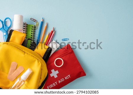 Yellow backpack with red first aid kit, bandage, sanitizer, pencils and notebooks arranged to represent school safety, health and emergency preparedness for students