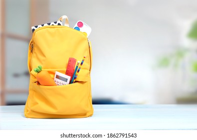 Yellow backpack with school supplies on wooden table empty copy space background.Knapsack with tools and accessories indoors.