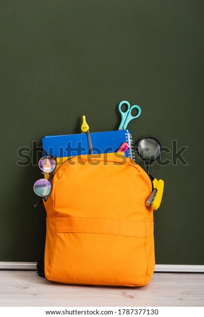 yellow backpack with school supplies on desk
near green chalkboard
