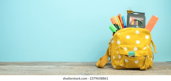 Yellow backpack with white polka dots with different colorful stationery on table. Blue background. Back to school. Banner design - Powered by Shutterstock