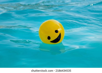 Yellow ball with a smiling face floating on blue water - Powered by Shutterstock