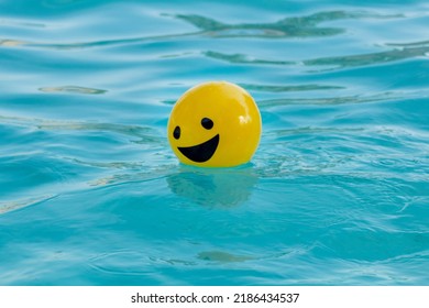 Yellow ball with a smiling face floating on blue water - Powered by Shutterstock