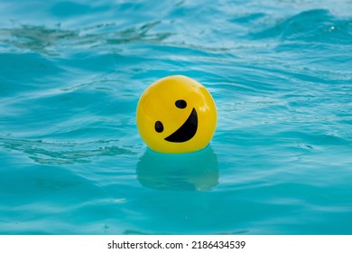 Yellow ball with a smiling face floating on blue water - Powered by Shutterstock