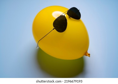 A yellow balloon with sungrasses on a blue surface