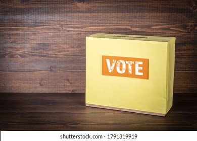 Yellow Ballot Box On A Wooden Background. Politics, Civic Duty, Choice And Belief Concept