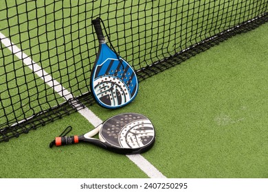 Yellow balls on grass turf near padel tennis racket behind net in green court outdoors with natural lighting. Paddle is a racquet game. Professional sport concept with copy space. - Powered by Shutterstock