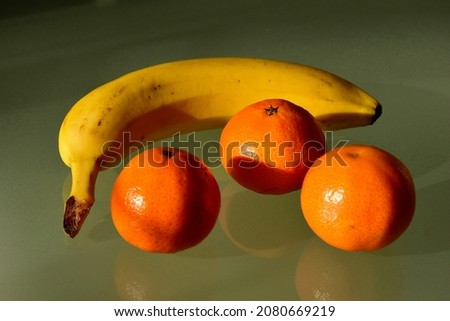 yellow banana and orange color clementines groupped. selective focus. closeup view. reflective surface. healthy eating. vitamin C, B and potassium. antioxides. tropical fruits. vegetarian lifestyle.
