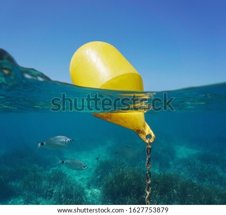 A yellow beacon buoy in the sea for beach marking and cross channel limits with blue sky and fish underwater, split view half over and under water surface, Mediterranean, Spain
