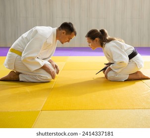 Judo de cinturón amarillo en judogi blanco y joven judo de cinturón negro en judogi blanco arrodillado 
