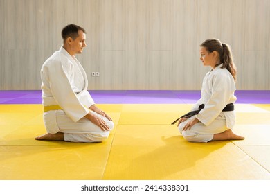 Yellow belt judo man in white judogi and young black belt judo girl in white judogi kneeling 