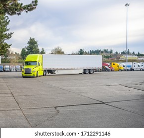 Yellow Big Rig Classic Bonnet Industrial Diesel Semi Truck With Refrigerator Semi Trailer Running On The Truck Stop Parking Lot Past Other Parked Trucks Looking For Empty Reserved Parking Spot