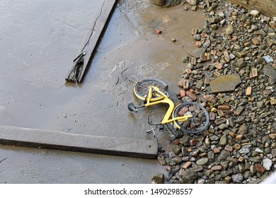 Yellow Bike Thrown Onto Mudflats Of Thames River. Also Planks Of Wood And Other Rubbish.