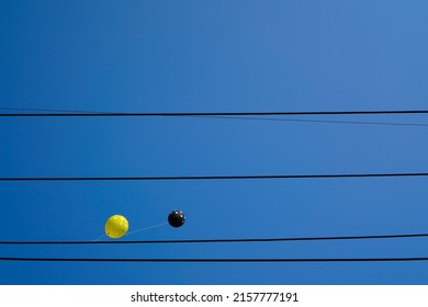 Yellow And Black Balloon Tethered To A Power Line On A Blue Sky Background