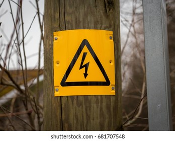 a yellow and black danger of death sign with triangle and lightening bolt on a wooden electric pole pylon outside resource with forest at the background