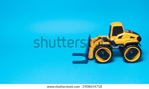 The yellow black forklift toy\
typewriter on a blue background. Construction equipment tractor for\
children for toy store, copyspace place for\
text.