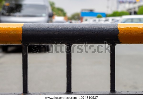 Yellow and black metallic fence with city\
background. Parking facility rail. Metallic border in yellow and\
black stripes. Prohibited entrance. Path block. Road dead end.\
Airport facility zone\
barrier