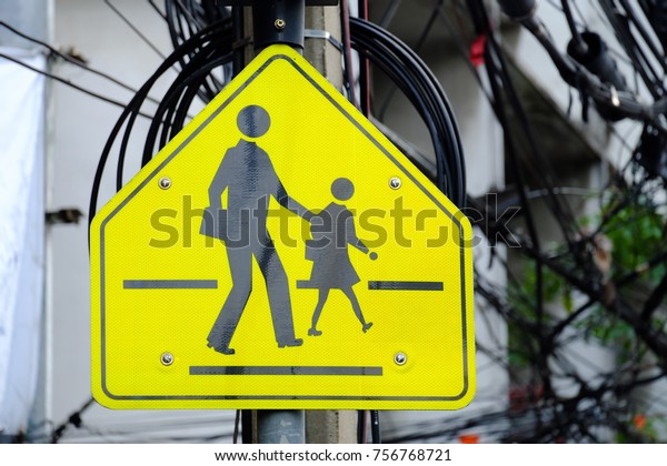 A\
yellow black sign of school zone on top of metal pole in the city\
with blur messy electricity wire and school\
building