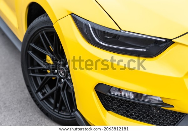 Yellow with black stripes Ford Mustang muscle car\
in a parking lot. Close-up of headlight and wheel. Russia,\
Rostov-on-Don 23 Oct2021