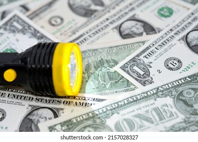 A yellow and black torch with a led light on a blurred background of American money banknote bills currency, USA dollars in a selective focus with a torch light, money and economy concept - Shutterstock ID 2157028327