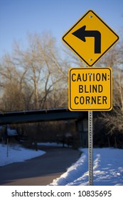 Yellow Blind Corner Turning Warning Sign On A Biking Trail With A Curve And A Bridge In Perspective