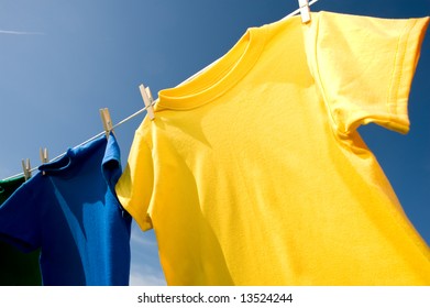 A Yellow And Blue Colored T-shirt Hanging On A Clothesline On A Beautiful, Sunny Day, Add Text Or Graphic To Shirts Or Copy Space