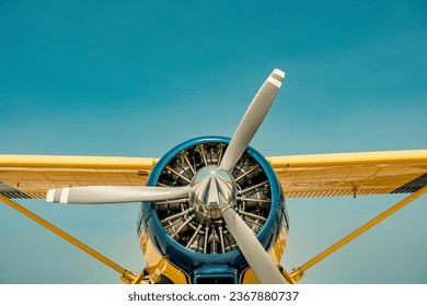 A yellow and blue float plane against a clear blue sky. A portion of the wings can be seen. The camera is centered on the nose and propeller.