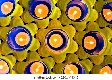 Yellow and blue flower tealight candle holders. Pretty background pattern image. Tessellating painted glass petals with lit tea light candles. Bright orange flames in beautiful bold floral design - Shutterstock ID 2201443345