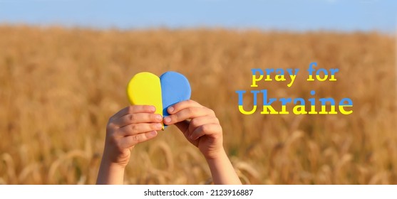 Yellow and blue heart in the hands of a child .Wheat field at sunset.Pray for Ukrain in colors of flag.Crisis in international relations, Russian military invasion of Ukraine