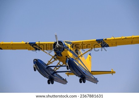 A yellow and blue high wing float plane powered by a radial engine on departure. Set against a clear blue sky.