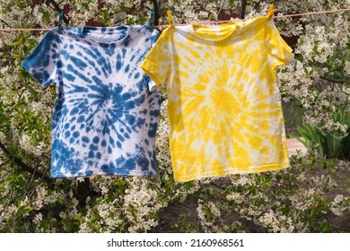 Yellow and blue tie dye T-shirts hang on a clothesline against the background of a flowering tree. Minimal fashion concept. - Powered by Shutterstock