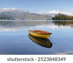 A yellow boat on the sea with a beautiful calming reflection of both the boat itself and the surrounding mountains 