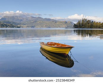 A yellow boat on the sea with a beautiful calming reflection of both the boat itself and the surrounding mountains 