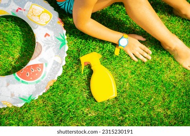 A yellow bottle of protective spray lies on the grass near with sitting child with a water park and pool bracelet - Shutterstock ID 2315230191