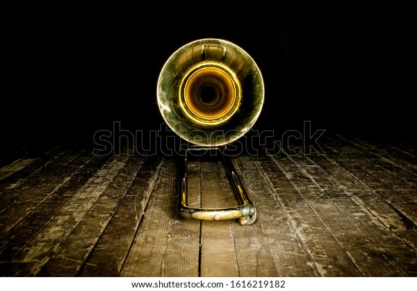 yellow brass instrument trombone\
lies on the wooden floor of the stage. front view on the\
bell
