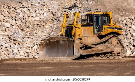 Yellow Bulldozer Working In Front Of A Large Pile Of Rock, Gravel, And Dirt