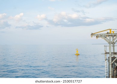 A yellow buoy floats in calm waters, with a metal platform to the right of the image. The sky is blue and filled with clouds. The scene is serene and tranquil. - Powered by Shutterstock