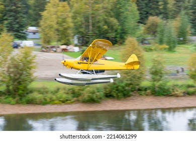 Yellow Bush Float Plane Flying Over River In Alaska