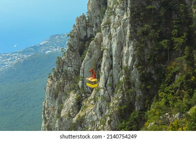 Yellow cabin of funicular against the background of the steep Ai-Petri cliff in the Crimea. A view of mountains, forest and sea from above. Cableway Miskhor-Sosnovy Bor-Ai-Petri. It was opened in 1988