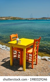 Yellow cafe restaurant table of street cafe with chairs on beach in Adamantas town on Milos island with Aegean sea with boats and yachts in background. Milos island, Greece